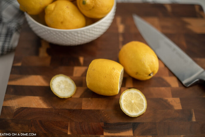 Close up image of a bowl of lemons. Two lemons on a cutting board with a knife and the ends cut off. 