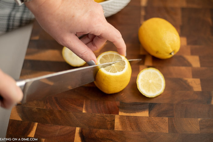 A close up image of a lemon being cut in half with a whole lemon on the side. 