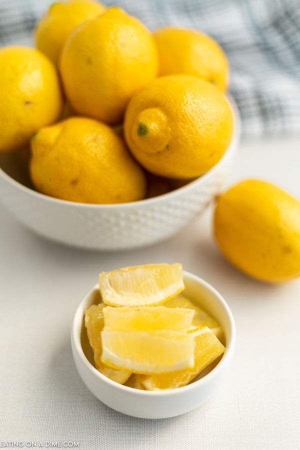 Close up image of a bowl of lemons with a small bowl of lemon wedges. 