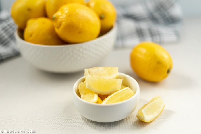 Close up image of a bowl of lemons with a small bowl of lemon wedges. 