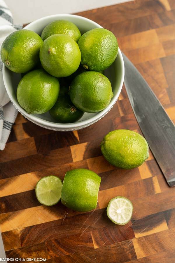 Close up image of a bowl of limes with a cutting board and knife. Lime with the ends cut off. 