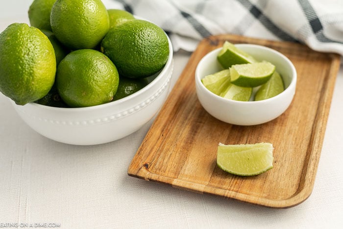 Close up image of a bowl of limes with a cutting board and a bowl of lime wedges. 