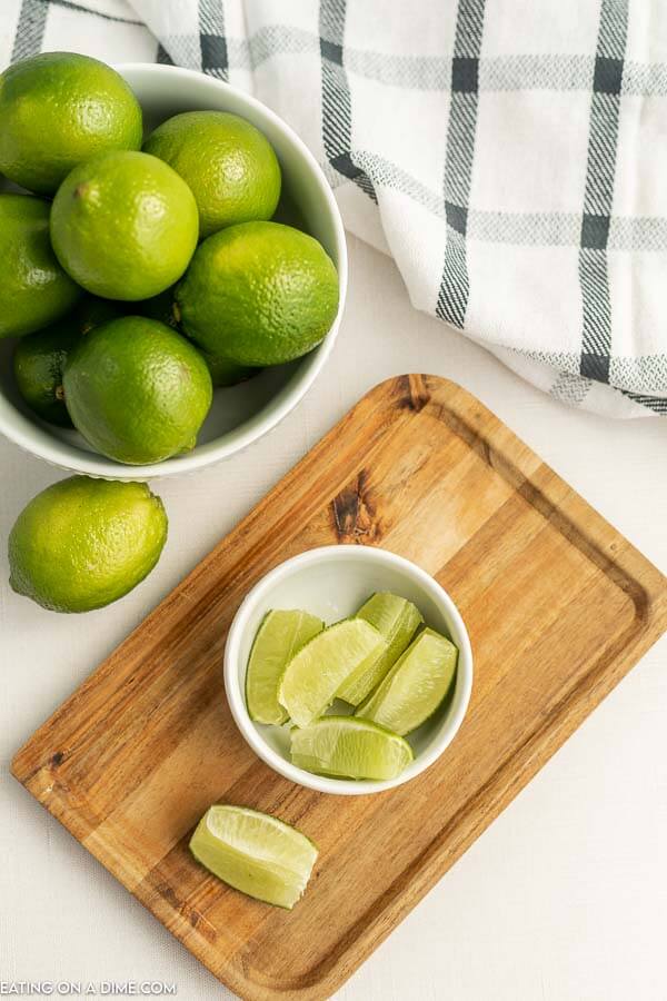 Close up image of a bowl of limes with a cutting board and a bowl of lime wedges. 