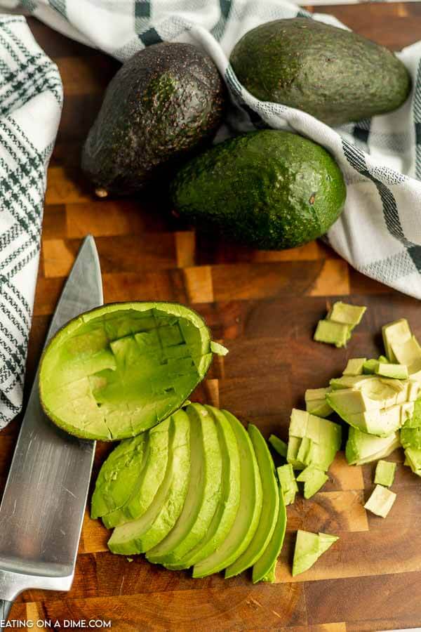 Close up image of sliced avocados with three whole avocados. 
