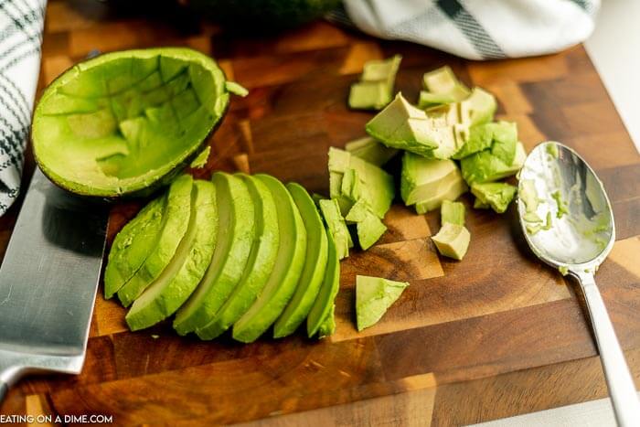 close up image of sliced and chopped avocado on a cutting board with a knife and spoon. 