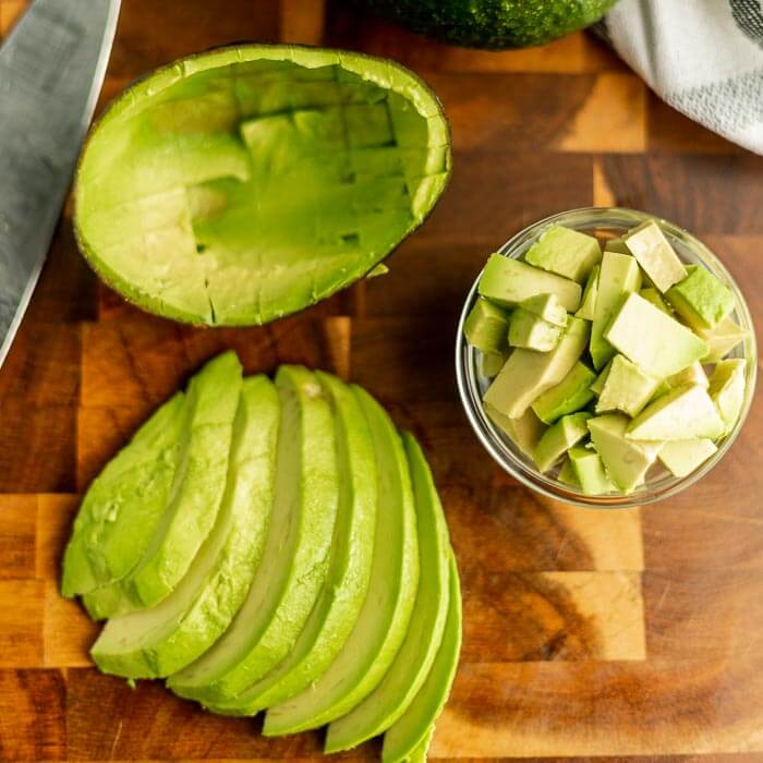 close up image of sliced and chopped avocado on a cutting board with a knife. 