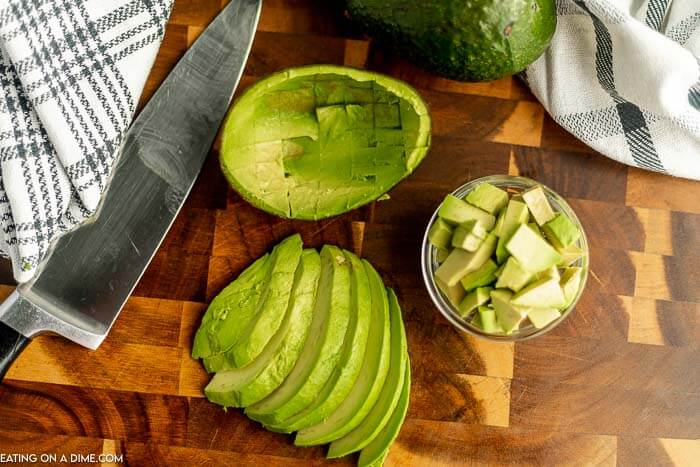 Close up image of sliced avocados with a knife on a cutting board. With chopped avocados in a clear bowl. 