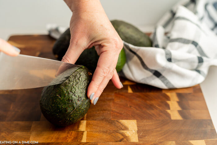 The process of beginning to slice a avocado with a knife on a cutting board. 