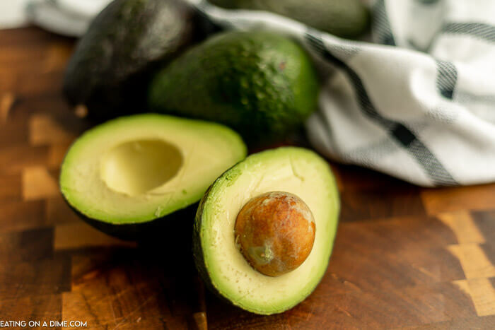 Close up image of sliced avocados with three whole avocados. 