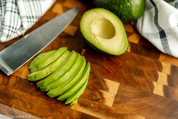 Close up image of sliced avocados with a knife on a cutting board. 