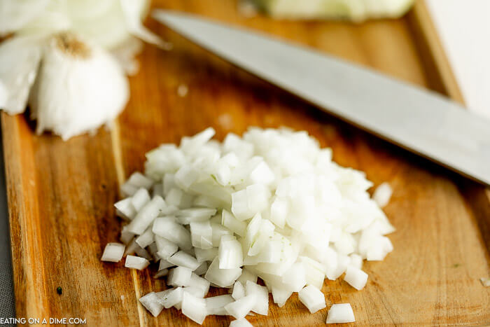 Close up image of diced onion on a cutting board with a knife. 