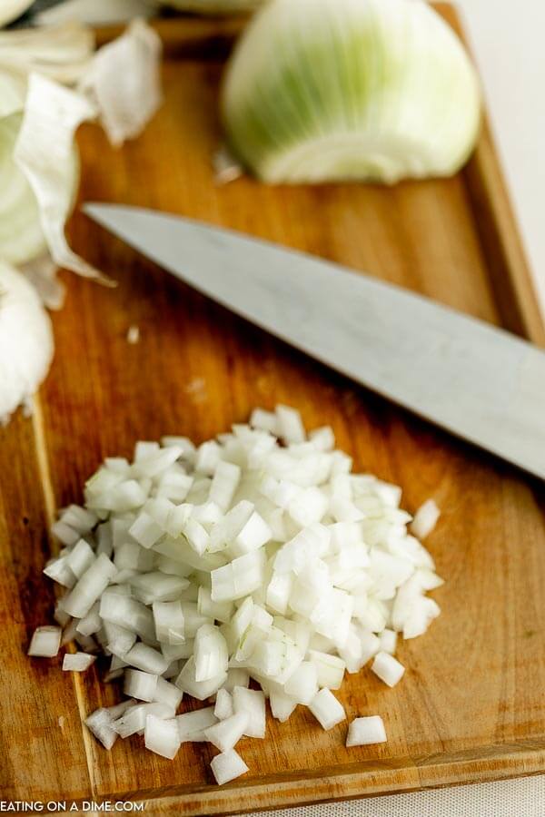 Close up image of diced onion on a cutting board with a knife. 
