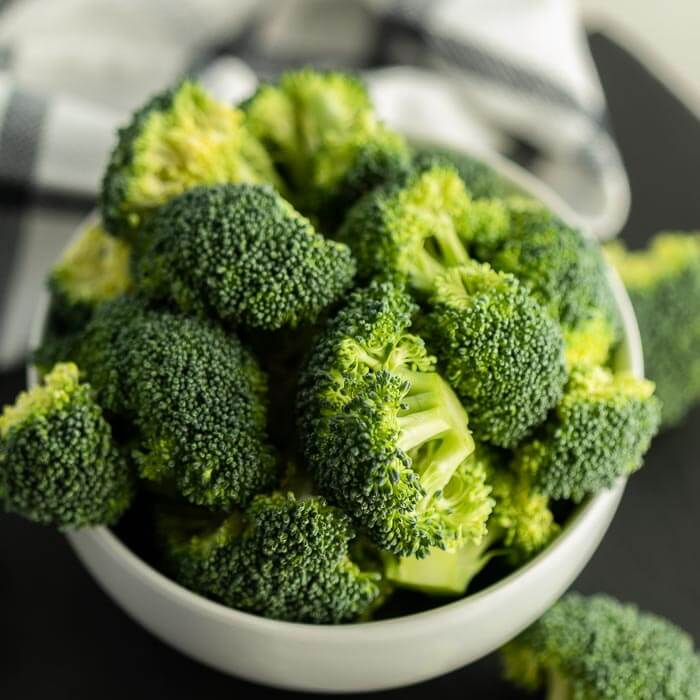 Close up image of a white bowl of cut broccoli. 