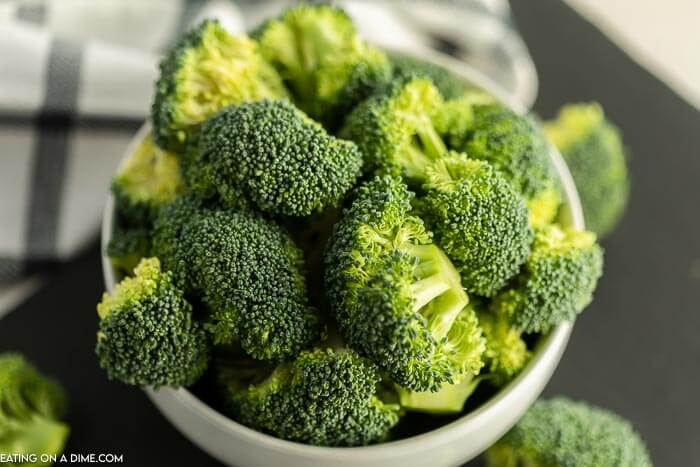 Close up image of a white bowl of cut broccoli. 