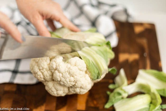 Whole Cauliflower being cut with a knife on a cutting board. 