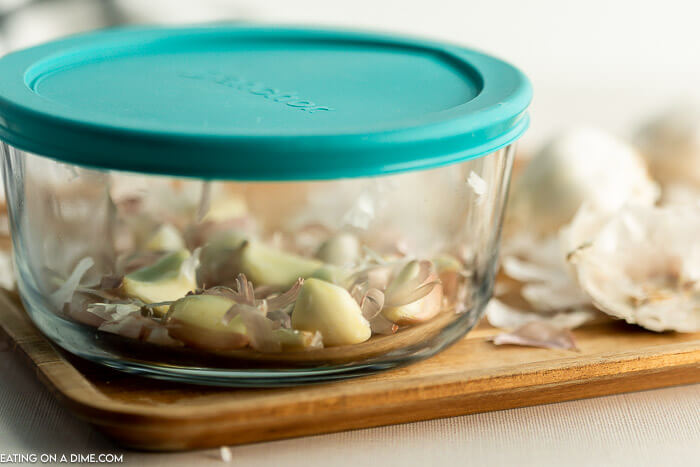 Close up image of garlic cloves and peeled garlic in a glass bowl with the peeling on the side. 