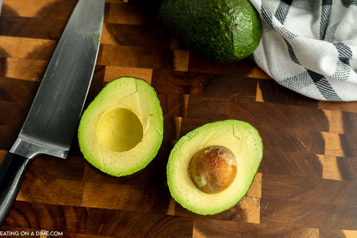 Close up image of an avocado in half with one whole avocados with a knife.