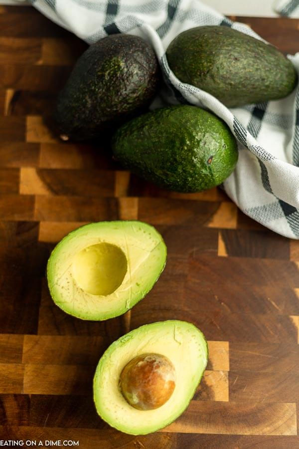 Close up image of an avocado in half with three whole avocados.