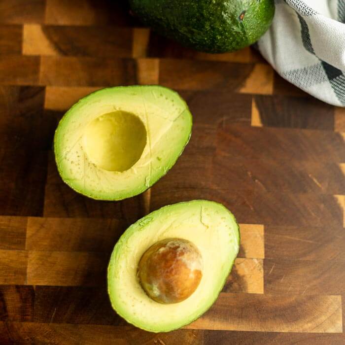 Close up image of an avocado in half with one whole avocados.