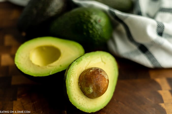 Close up image of an avocado in half with two whole avocados.