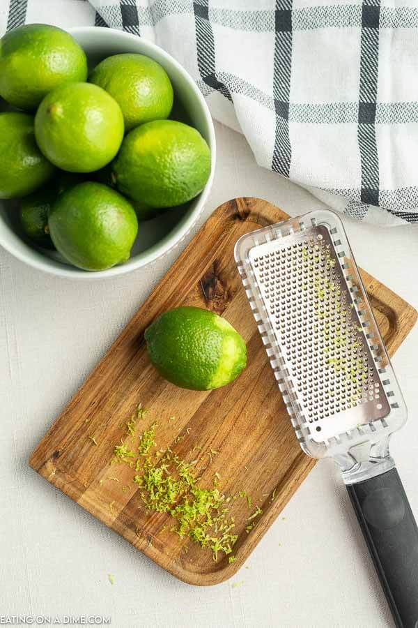 Close up image of a bowl of limes with a cutting board and a zester. 