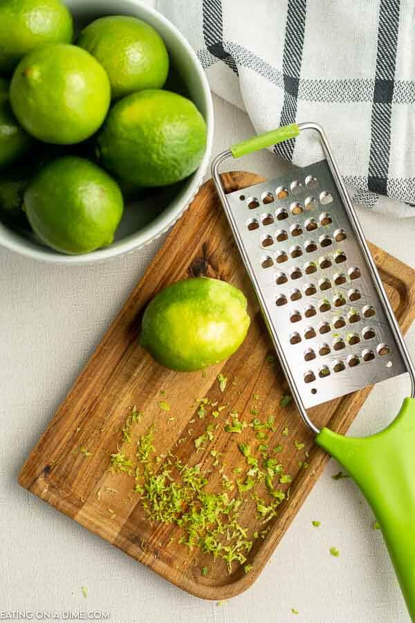 Close up image of a bowl of limes with a cutting board and a grater