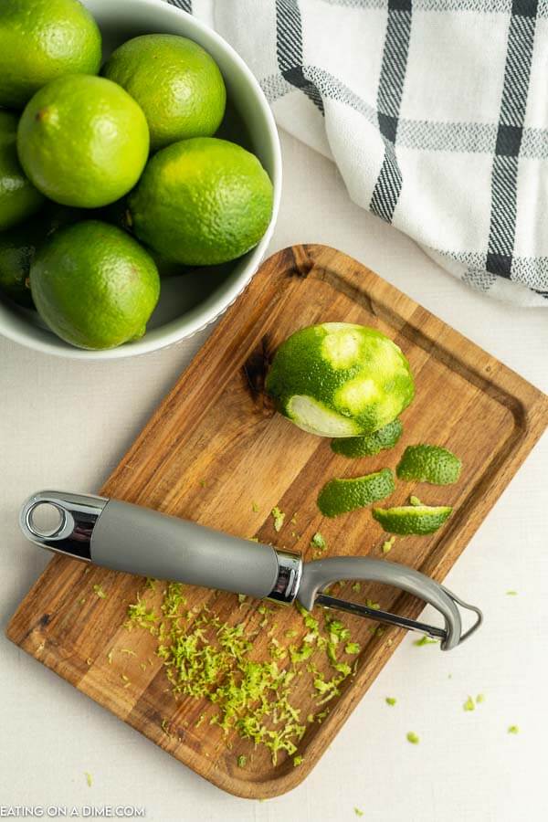 Close up image of a bowl of limes with a cutting board and a zester. 