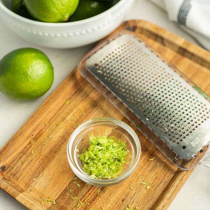 Close up image of a bowl of limes with a cutting board and a zester. 
