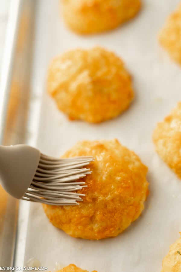 Close up image of Keto Biscuits being brushed with butter on a baking sheet. 