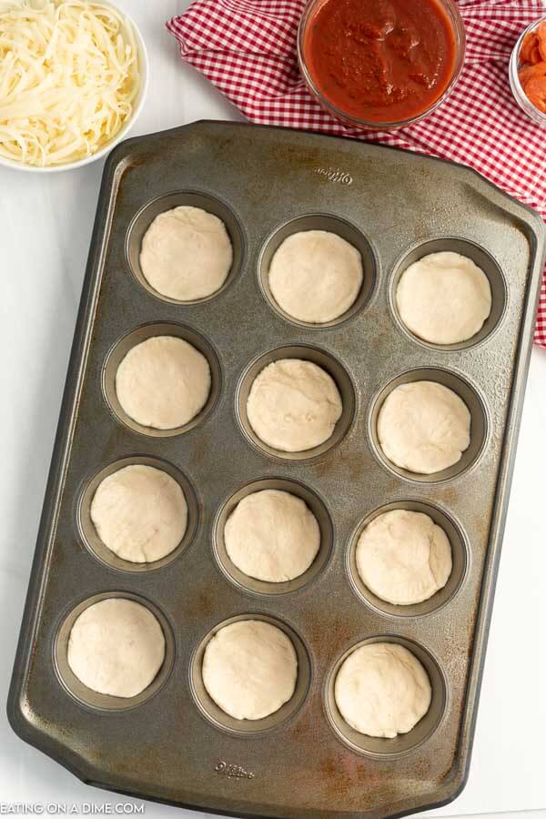 Uncooked biscuits flattened in a muffin tin. 