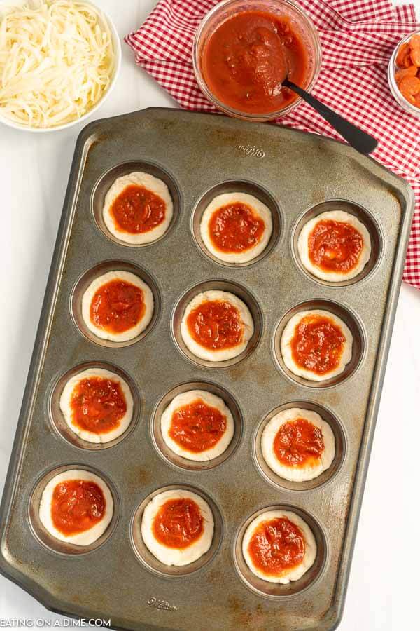 Uncooked pizza cupcakes in a muffin tin with biscuits and pizza sauce 