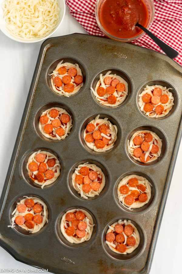 Close up image of uncooked pizza cupcakes topped with pepperoni in a muffin pan 