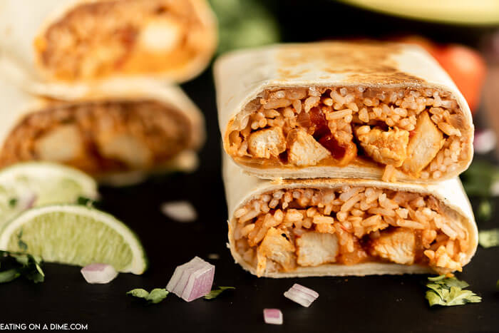 Close up image of chicken and rice burritos stacked with a side of lime. 