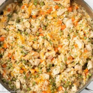 Close up of a chicken and rice mixture with peas and carrots topped with shredded cheese.