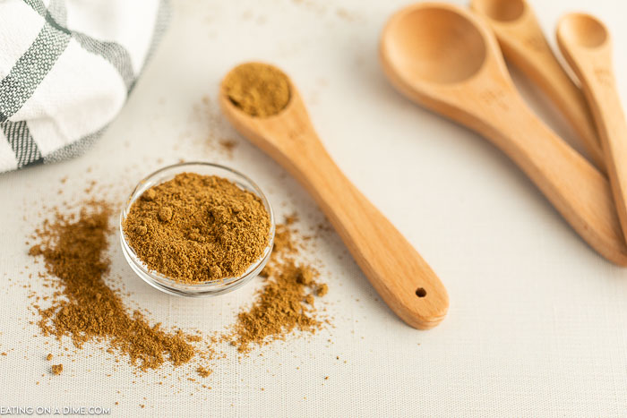 Close up image of ground cumin in a jar with teaspoons to the side. 