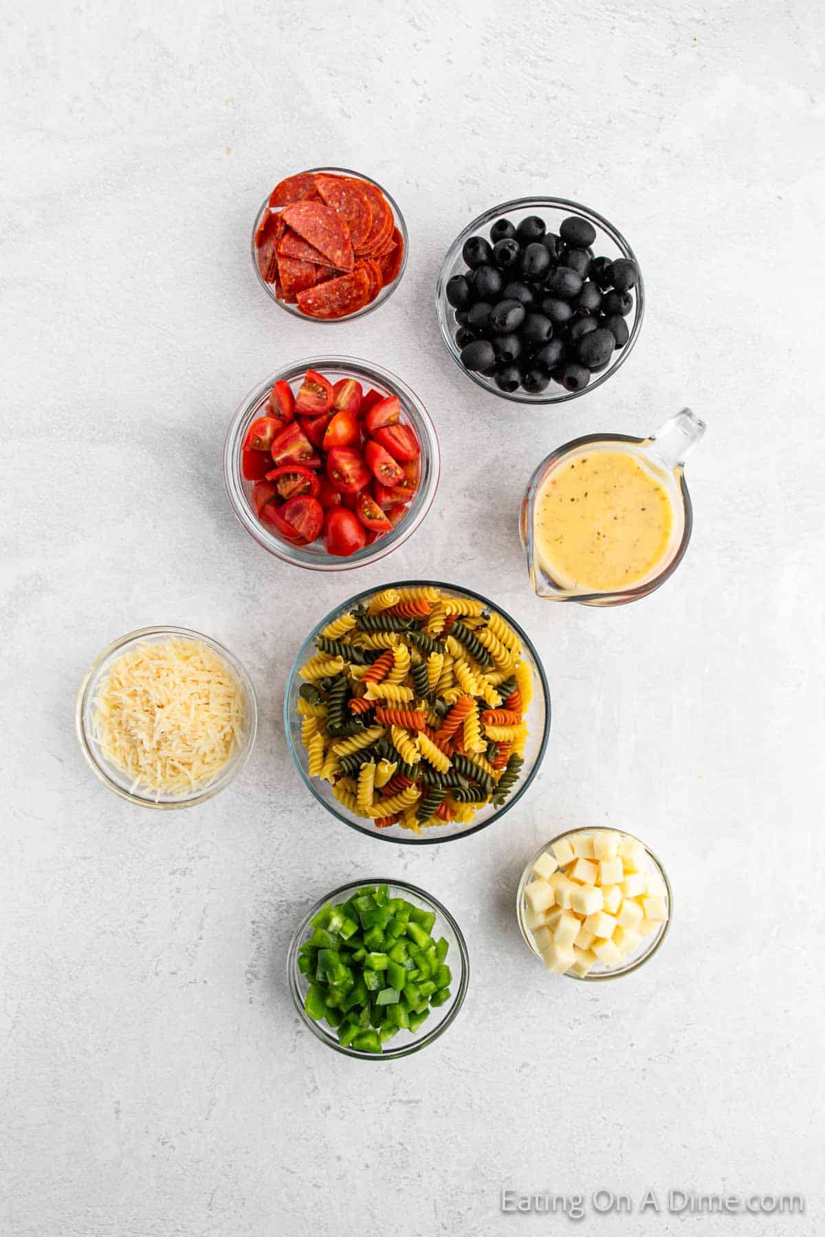 Italian Pasta Ingredients - Slice Pepperoni, black olives, cherry tomatoes, dressing, pasta, shredded parmesan cheese, chopped bell peppers, and cheese cubes