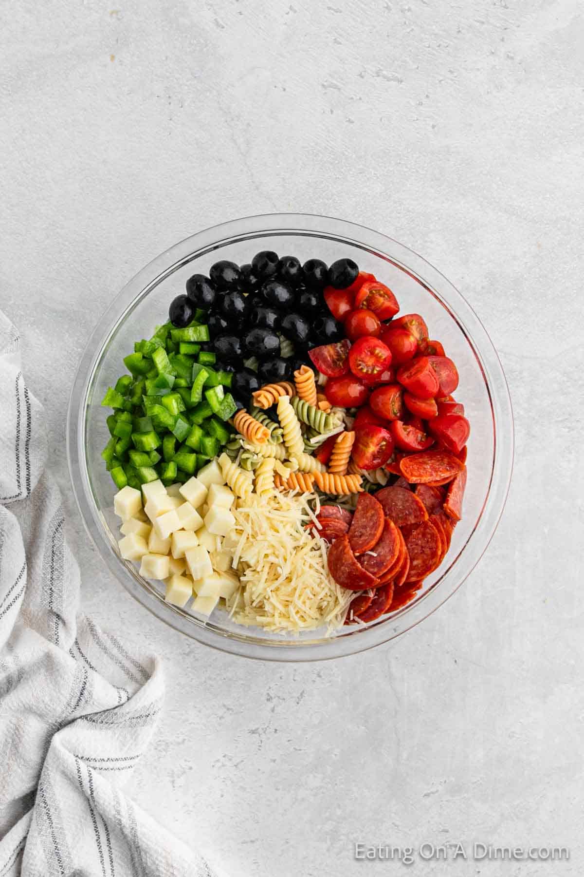 Chopped green onions, black olives, cherry tomatoes, slice pepperonis, pasta, cheese in a bowl
