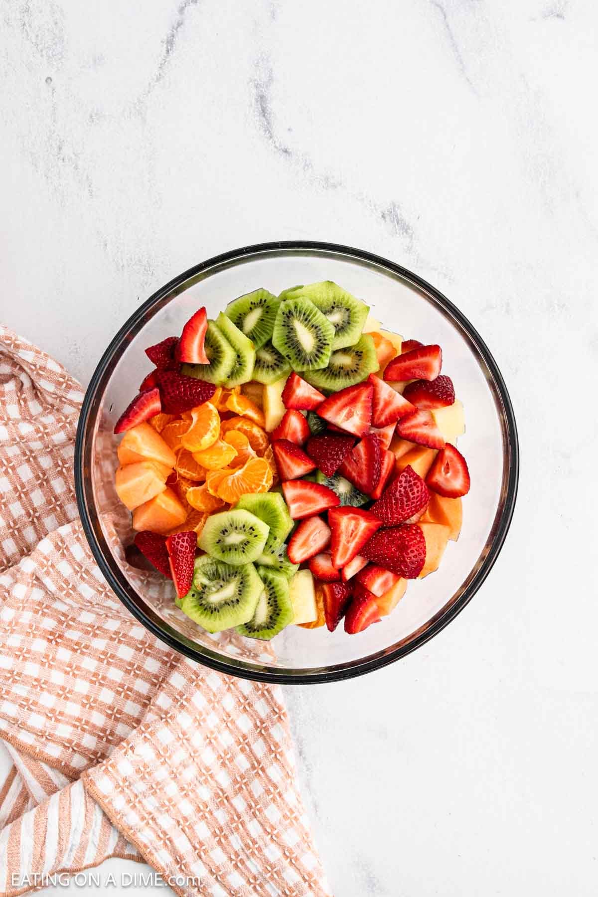 Fresh cut up strawberries, kiwi, oranges, and cantaloupe mixed together in a bowl.