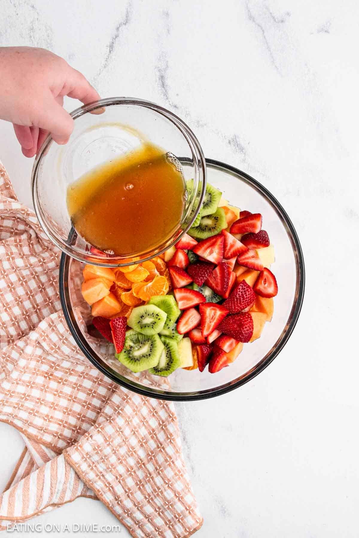 Pouring the honey dressing over the bowl of cut up fresh fruit.