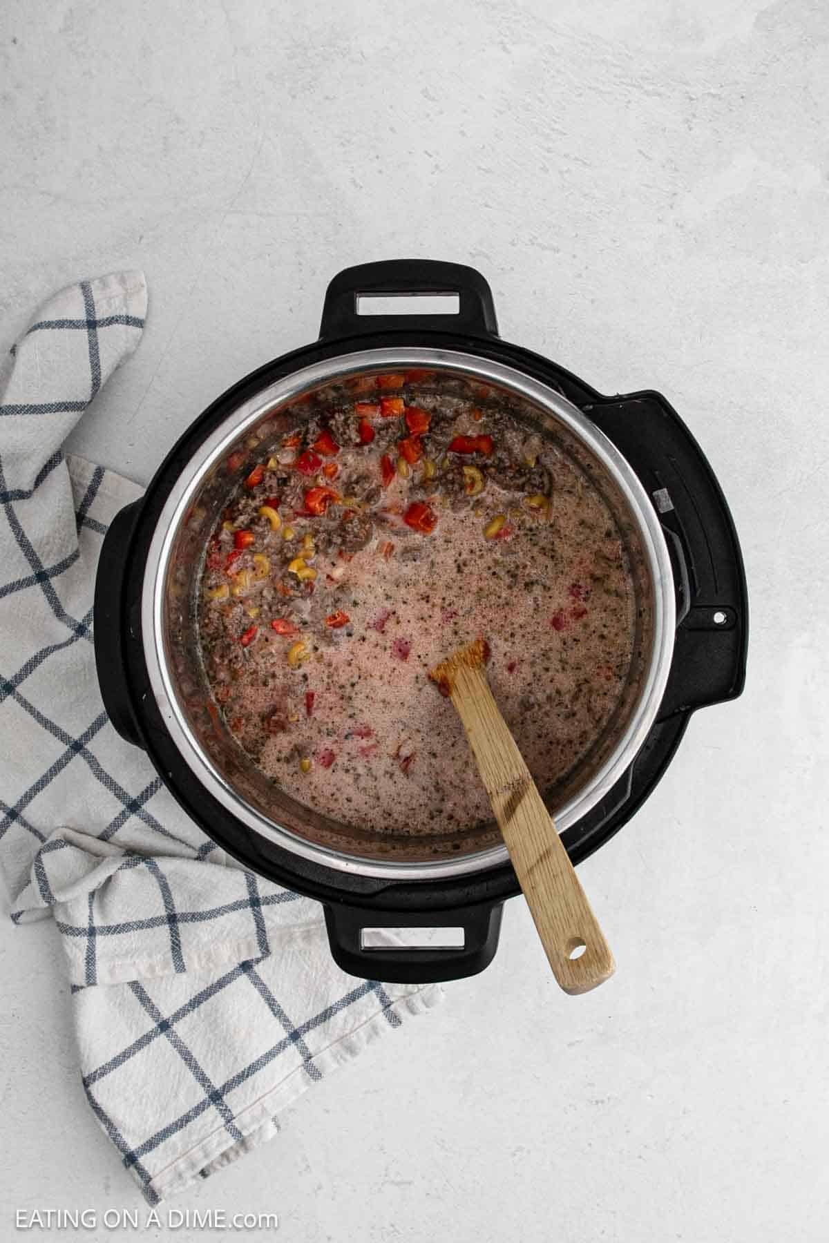 Combining the ingredients in the instant pot with a wooden spoon.