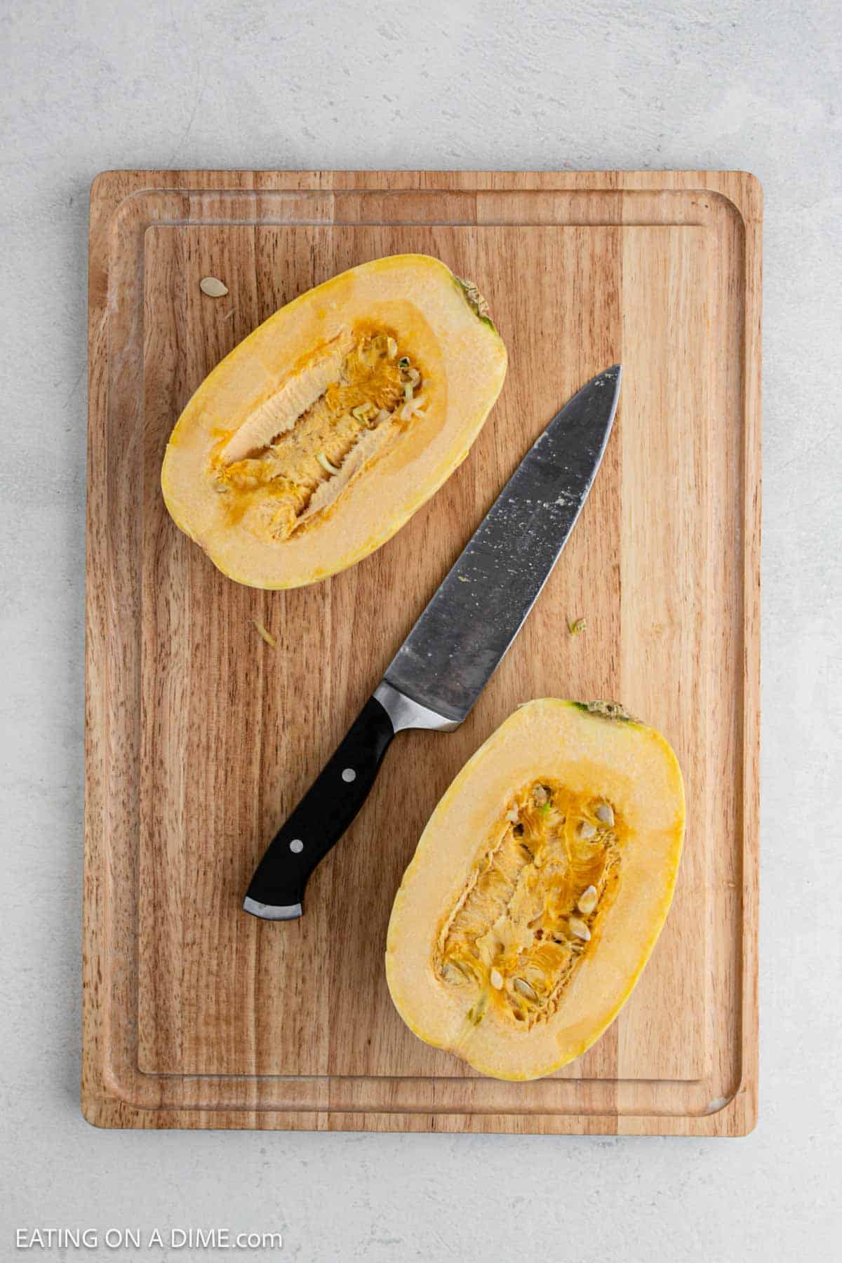 Squash cut into half on a cutting board with a knife nearby.