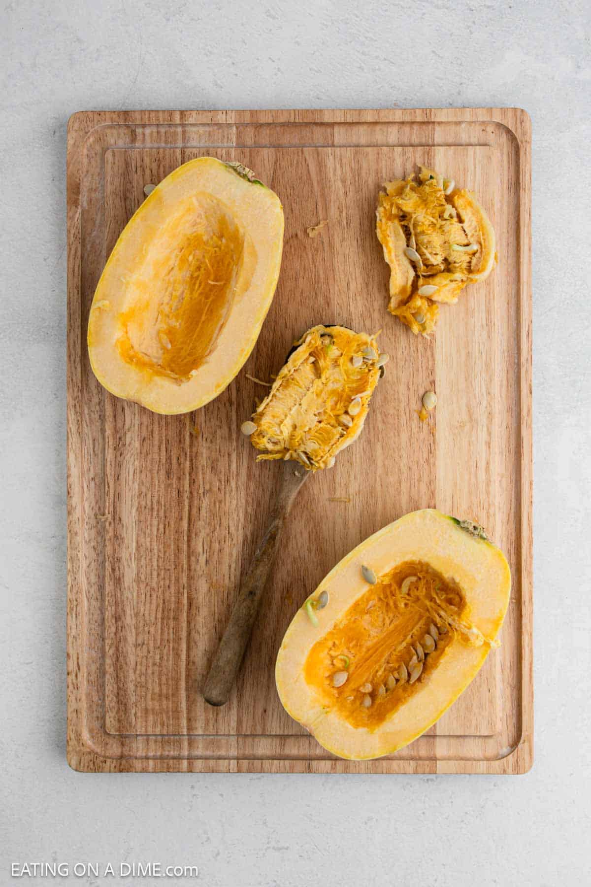 Fresh squash cut in half with the seeds being removed on a cutting board.