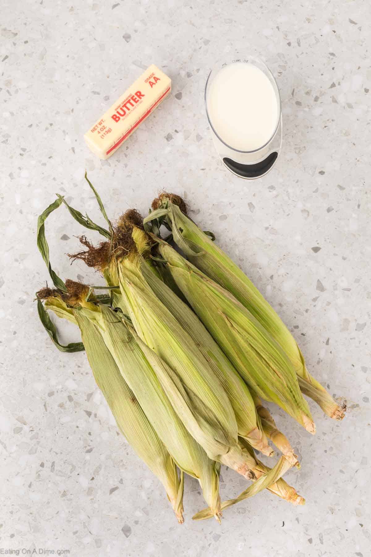 Stick of butter, cut of milk and corn on the cob covered with husks