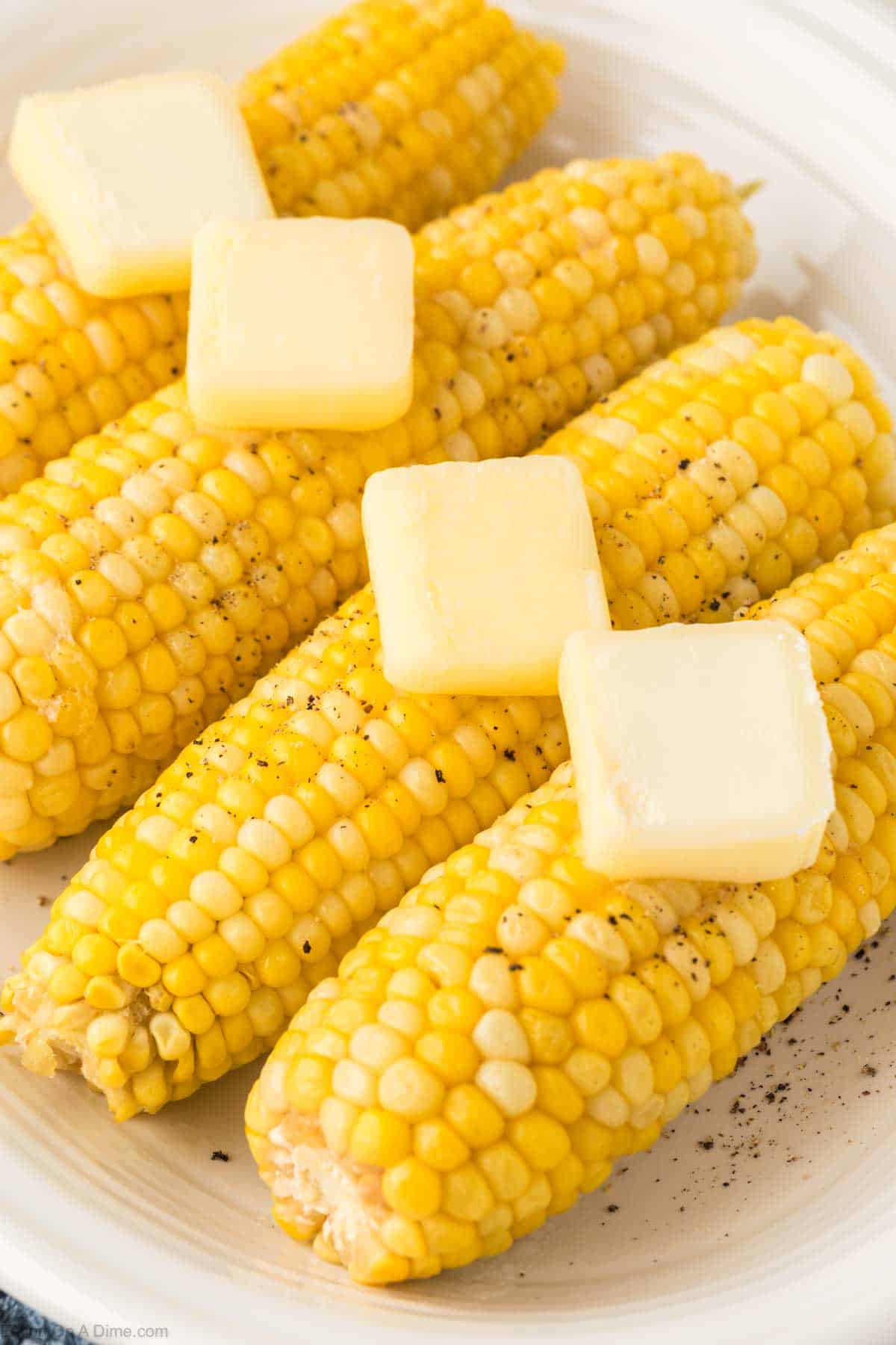 Corn on the cob placed on a platter topped with slice butter and salt and pepper