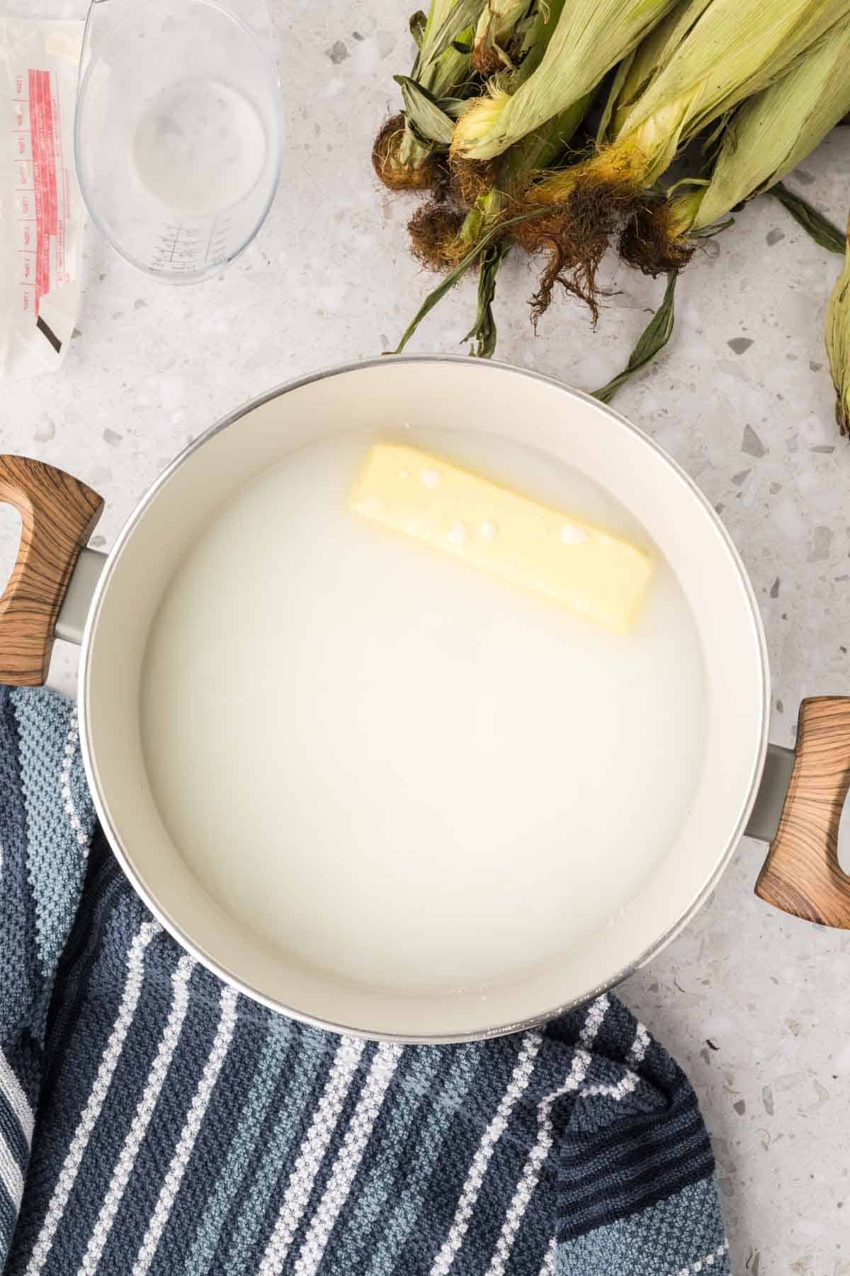 Large pot of water, milk and stick of butter with corn on the cob on the side