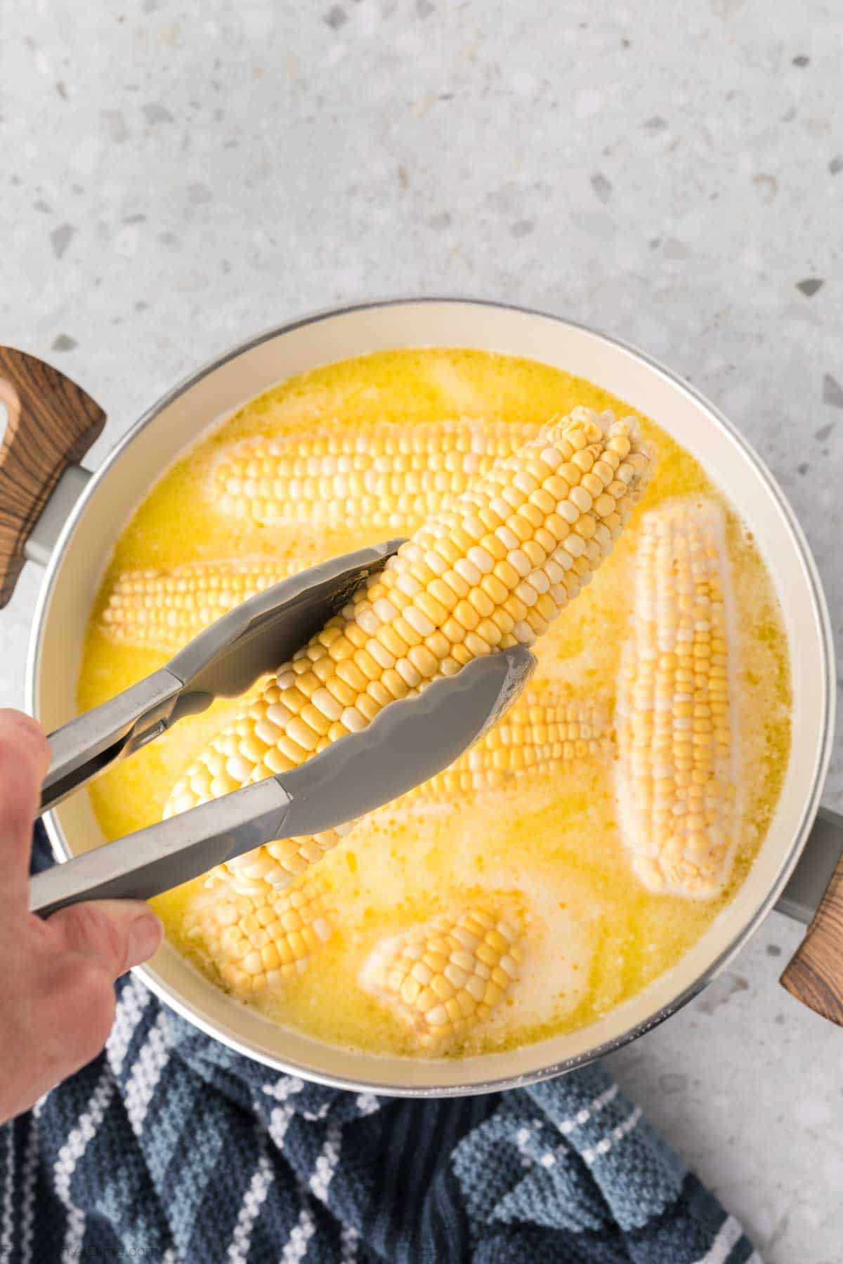 Corn on the cob placed in a large pot of melted butter and milk 