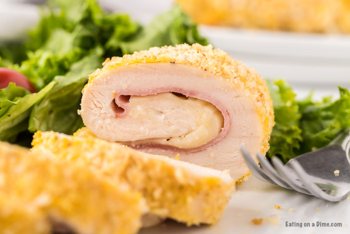 Close up image of chicken cordon bleu on a white plate with a side salad. 