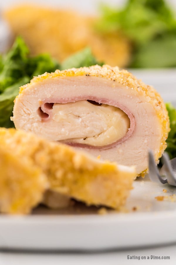 Close up image of chicken cordon bleu on a white plate with a side salad. 