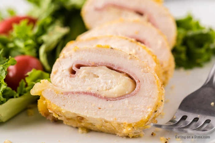 Close up image of chicken cordon bleu on a white plate with a side salad.