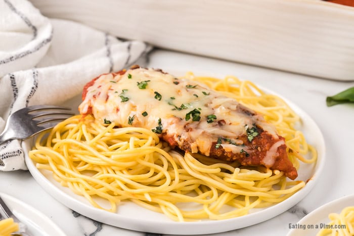 Chicken Parmesan on a white plate over pasta. 